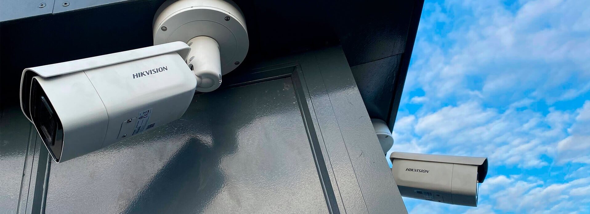 Ein Bild, das zwei Überwachungskameras bei einem Gebäude zeigt.